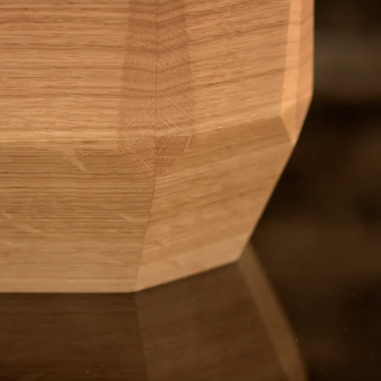 Künstlerisch gestaltete Holzurne mit gestapelten, unregelmäßigen Holzschichten und einer Applikation aus Moos. Ansicht im Detail - oben.