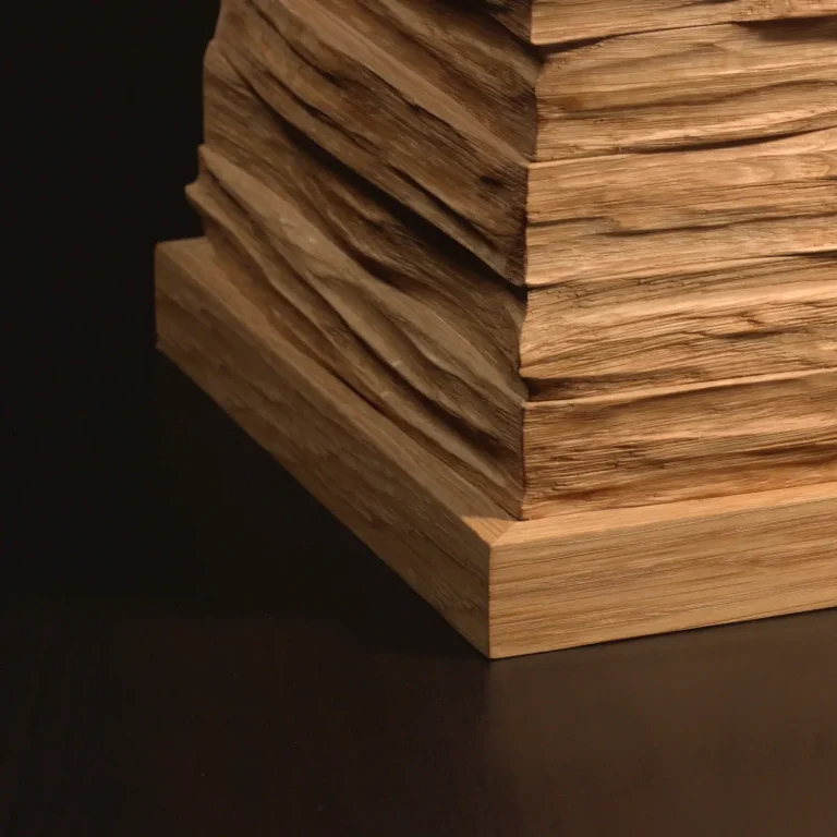 Künstlerisch gestaltete Holzurne mit gestapelten, unregelmäßigen Holzschichten und einer Applikation aus Moos. Ansicht im Detail - unten.