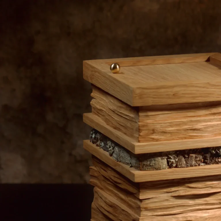 Künstlerisch gestaltete Holzurne mit gestapelten, unregelmäßigen Holzschichten und einer Applikation aus Moos. Ansicht im Detail - seitlich