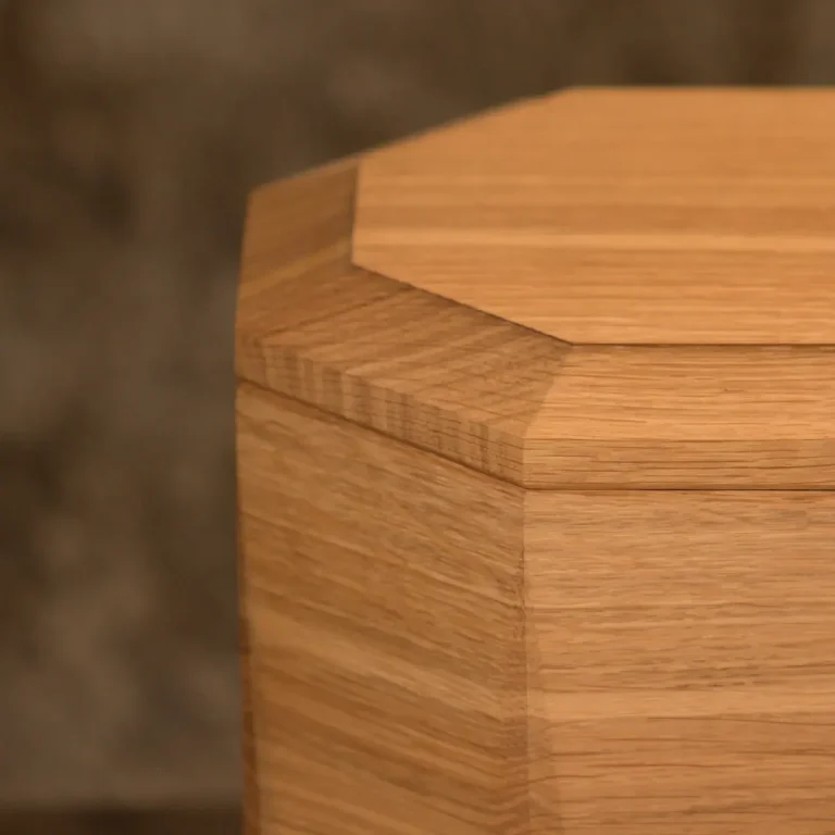 Eichenholzurne mit sechseckigem Körper und Facettenschliff an den Längskanten, glatter Oberfläche. Urne verjüngt sich im unteren Bereich. 