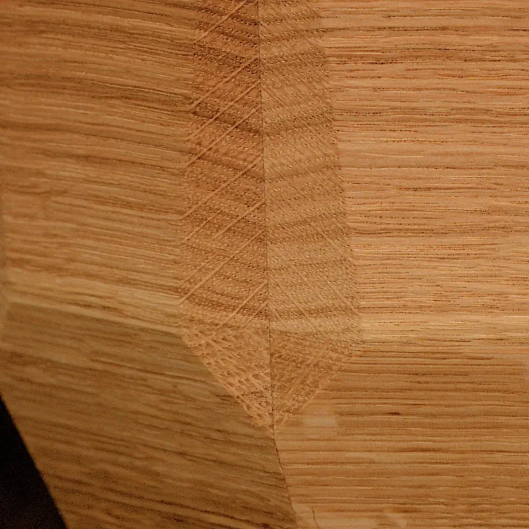 Künstlerisch gestaltete Holzurne mit gestapelten, unregelmäßigen Holzschichten und einer Applikation aus Moos. Ansicht im Detail - unten.