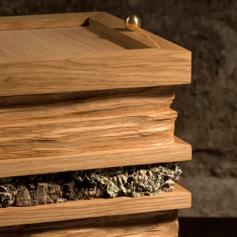 Künstlerisch gestaltete Holzurne mit gestapelten, unregelmäßigen Holzschichten und einer Applikation aus Moos. Ansicht im Detail - oben.